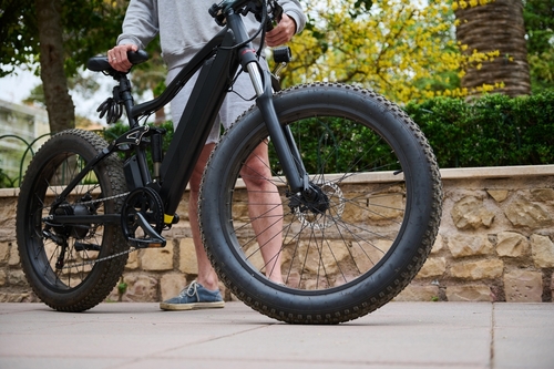 Rider walking with electric fat-tire e-bike on sidewalk in Florida – personal injury and e-bike accident risk