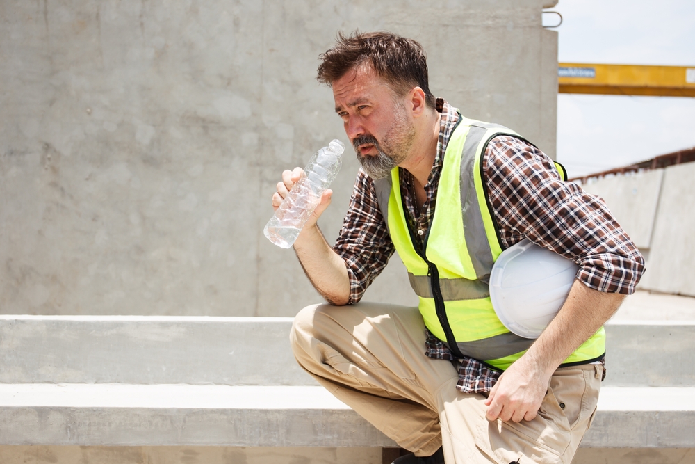 Construction worker showing signs of heat exhaustion while resting and drinking water outdoors in Florida summer heat
