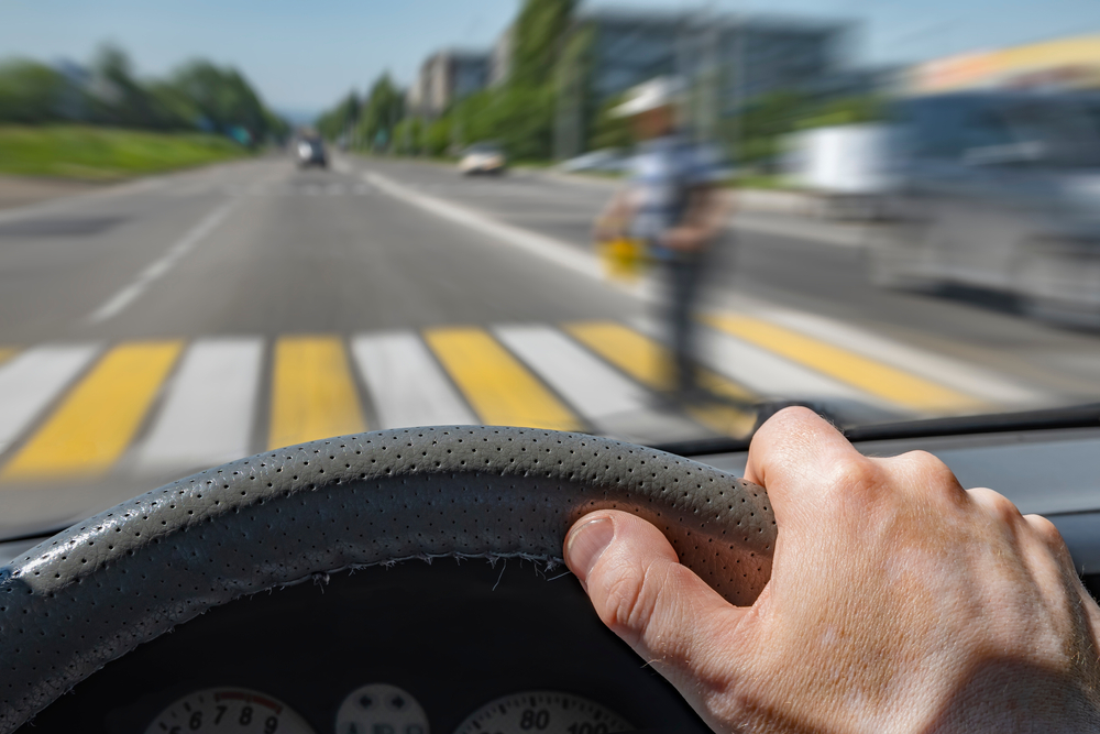 Driver hand on the steering wheel of a car moving at a high rate of speed about to hit a pedestrian